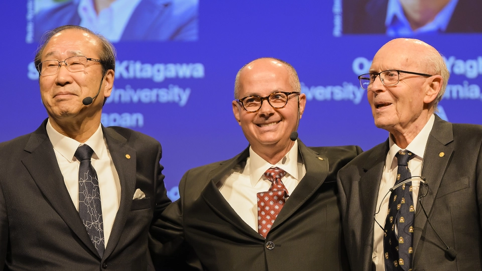 北川進博士、Omar M. Yaghi博士、Richard Robson博士の3氏。講堂をバックに寄り添い、笑顔で腕を組んでなごやかな雰囲気です。